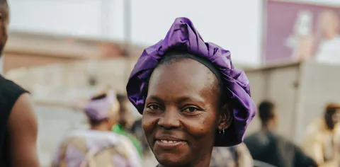 A woman in a colorful headwrap smiling at a market.