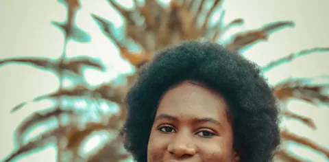 A young woman smiling outdoors under palm trees.