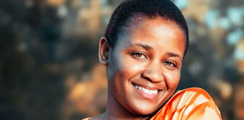 A woman in an orange top smiling outdoors.