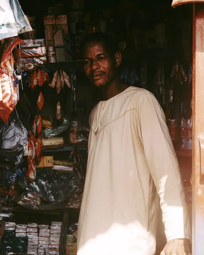 A trader in traditional attire standing inside a busy market stall in Abuja.