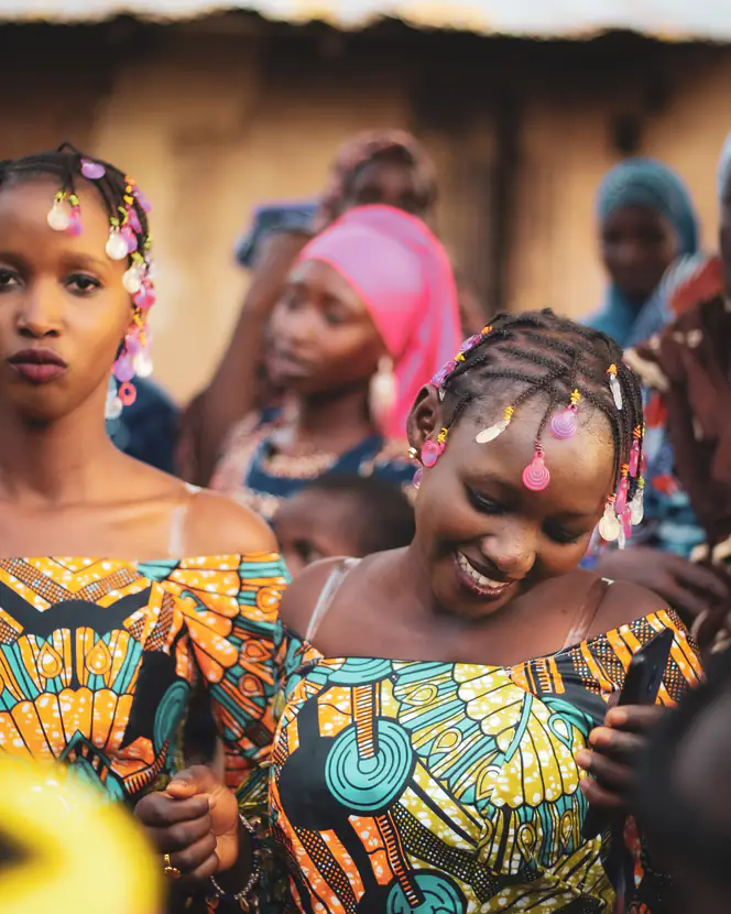 Women in brightly printed dresses dancing together at a celebration.