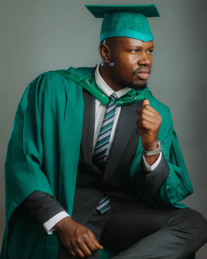 A graduate in green academic regalia and mortarboard, seated.