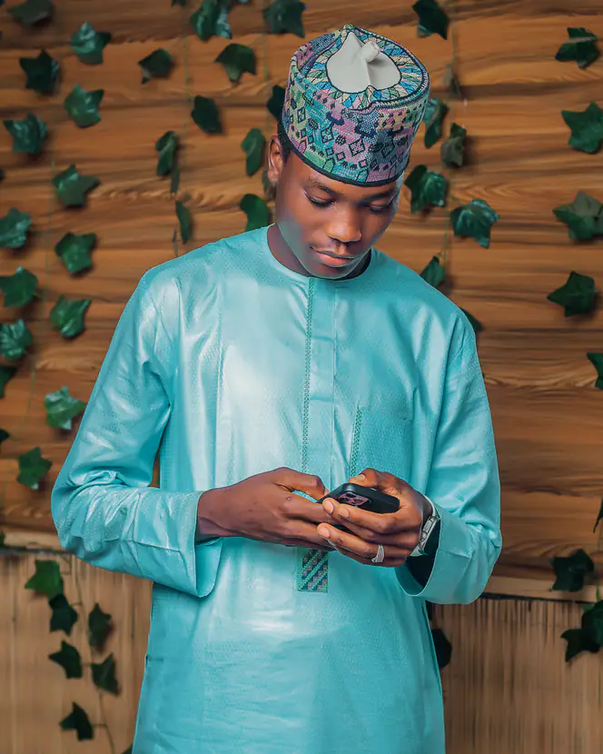 A young man in blue traditional attire using a mobile phone.