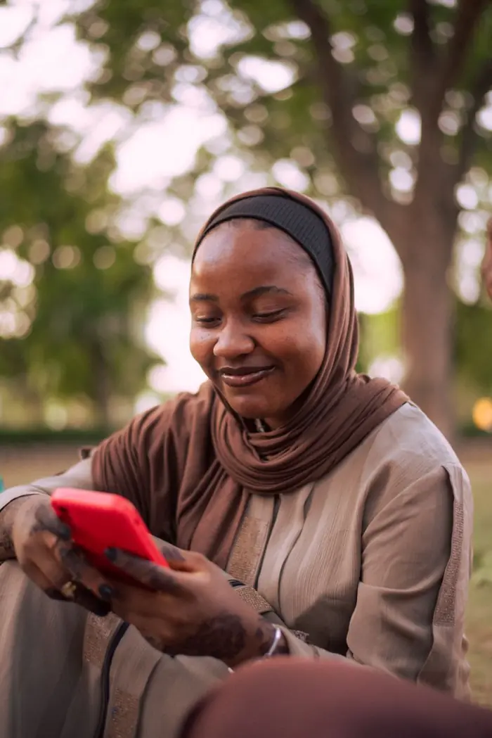 A woman smiling at her phone in a park in Zaria, Nigeria.