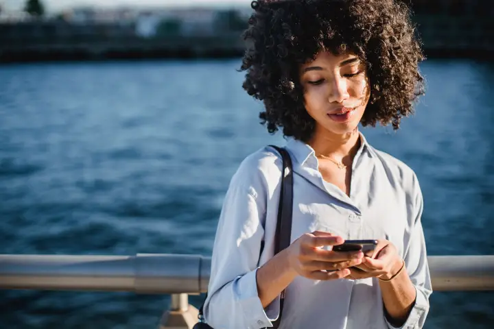 Woman using her phone beside the waterfront.